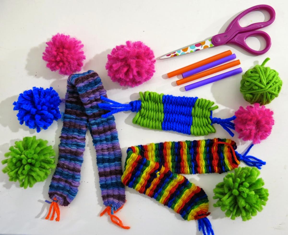 yarn, small woven scarves, handmade pom-poms, and scissors