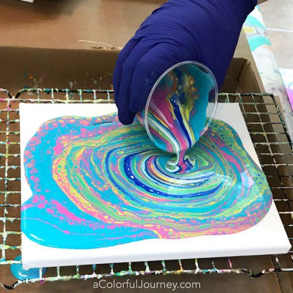 gloved hand pouring paint over canvas